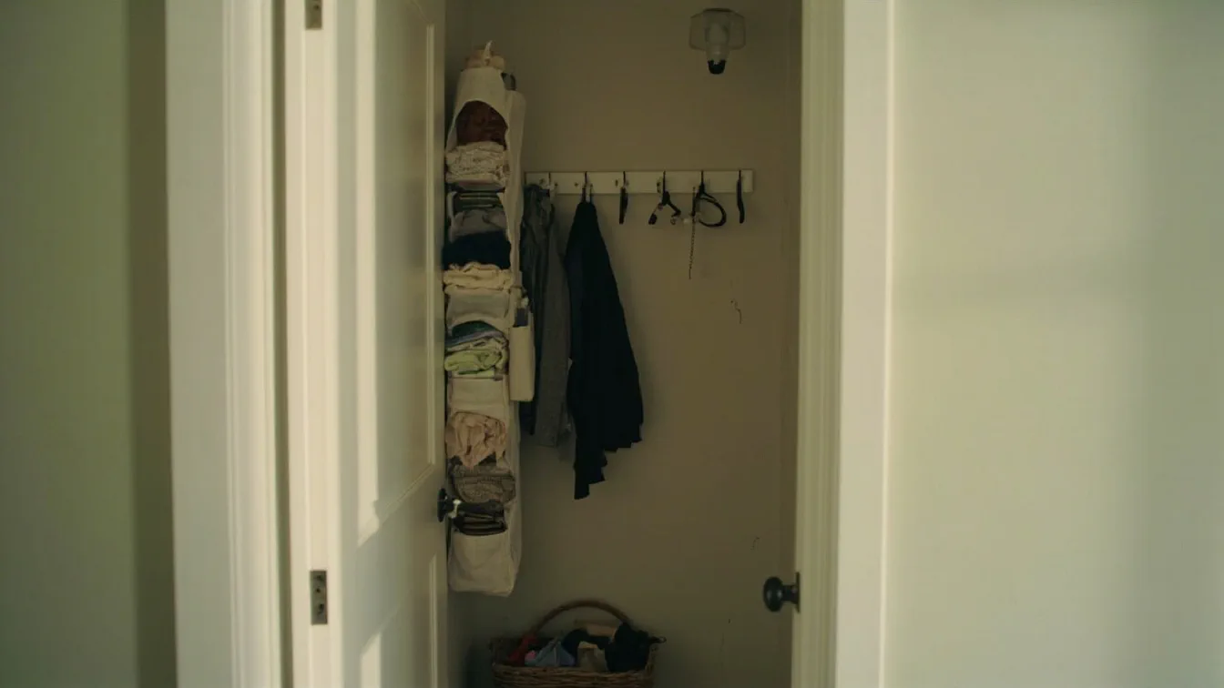 A narrow apartment entryway with a tall 5-shelf over-the-door organizer hung on a closet door by tension hooks, the pockets filled with sneakers and sweaters, a 9-hook rail below catching two jackets, and a woven basket on the floor for keys and a wallet — the rental wall behind the door visibly undamaged.